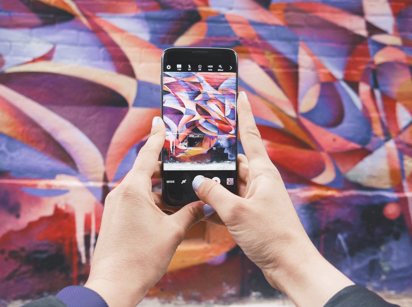 Hands of a person taking a photo of a pink graffiti with their phone