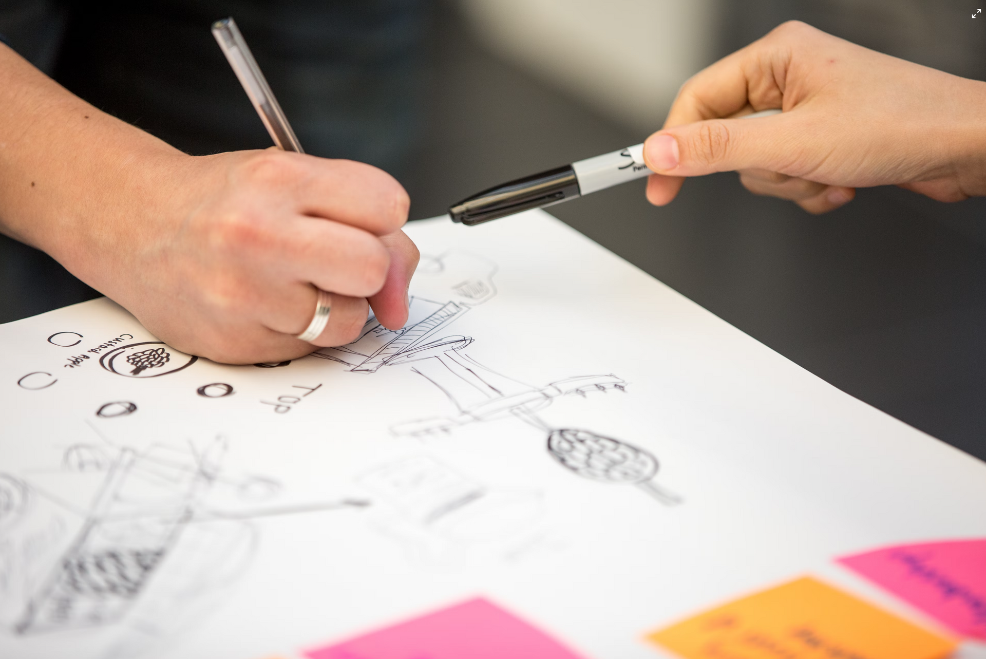 Close up on people's hands holding pens and sketching concepts on paper